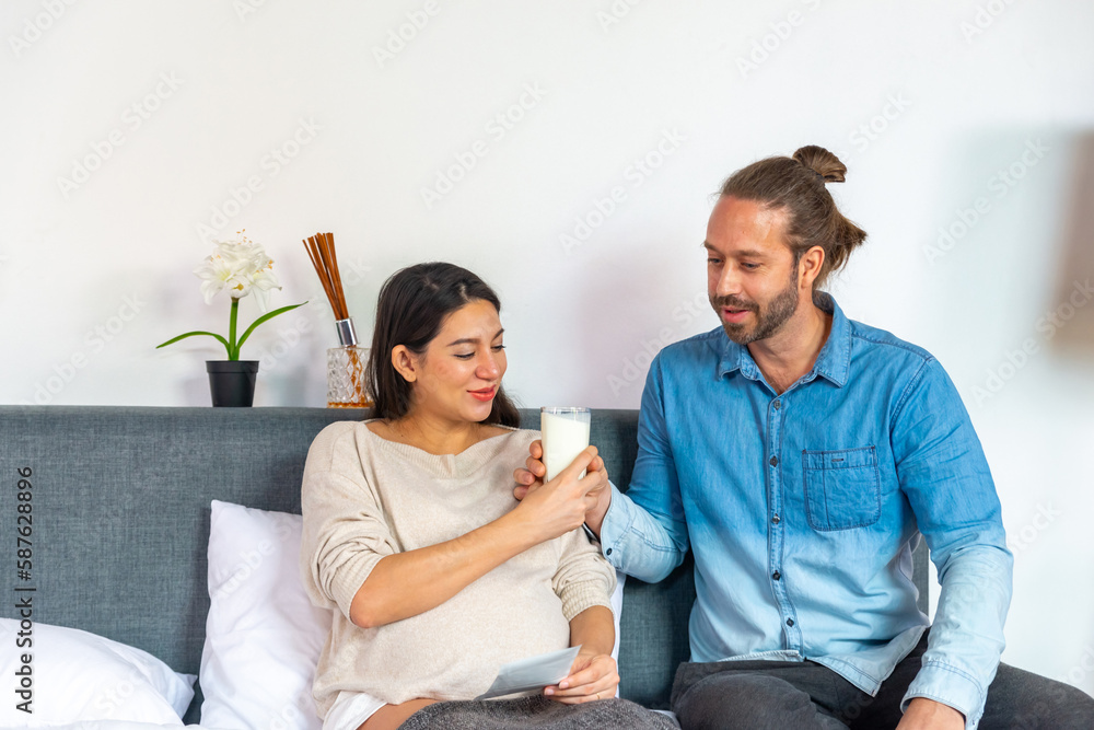 Caucasian pregnancy woman drinking fresh milk during looking ultrasound photo of her newborn baby with husband on the bed in bedroom. Family relationship and pregnant maternity health care concept. Caucasian pregnancy woman drinking fresh milk during looking ultrasound photo of her newborn baby with husband on the bed in bedroom. Family relationship and pregnant maternity health care concept.