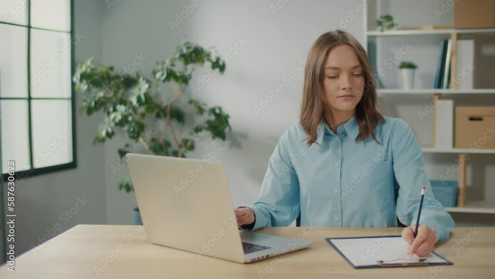 A Successful Young Woman is Writing Something While Working on the Computer. Organization of the Workspace at Home. Remote Work as a Way to Increase Productivity. A Successful Young Woman is Writing Something While Working on the Computer. Organization of the Workspace at Home. Remote Work as a Way to Increase Productivity.