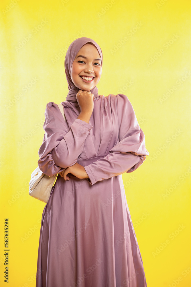 smiling Asian muslimah woman wearing pink dress on yellow background smiling Asian muslimah woman wearing pink dress on yellow background