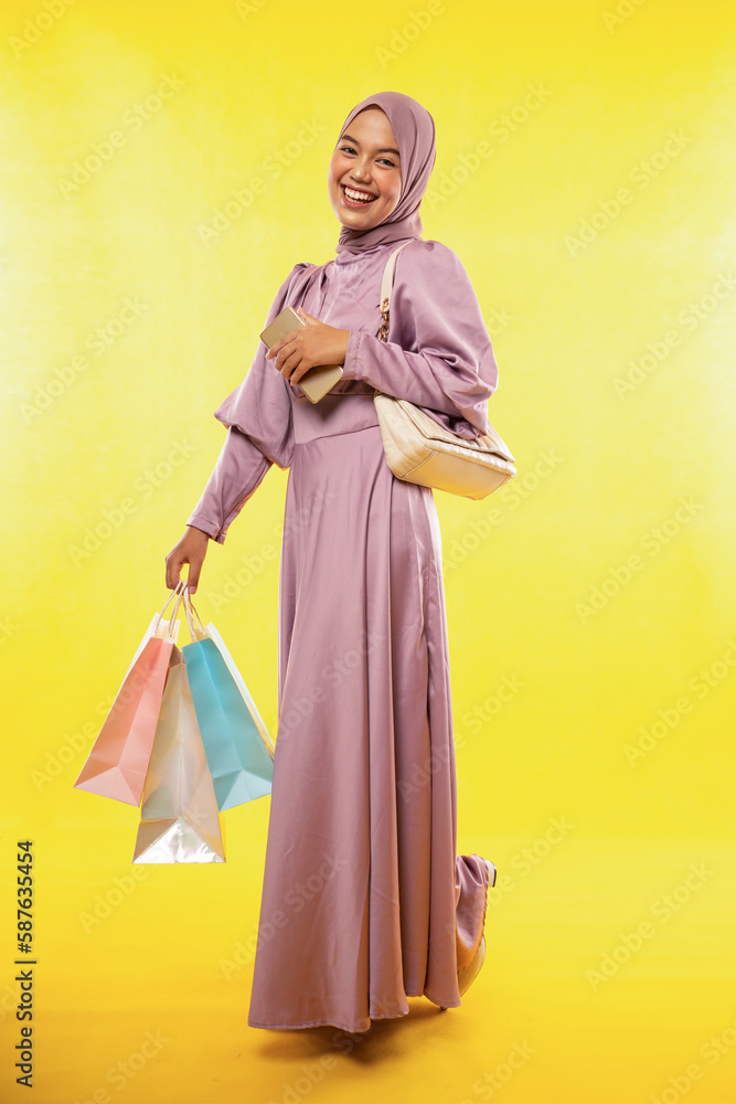 beautiful asian woman wearing color dress with hijab while shopping, isolated yellow background beautiful asian woman wearing color dress with hijab while shopping, isolated yellow background