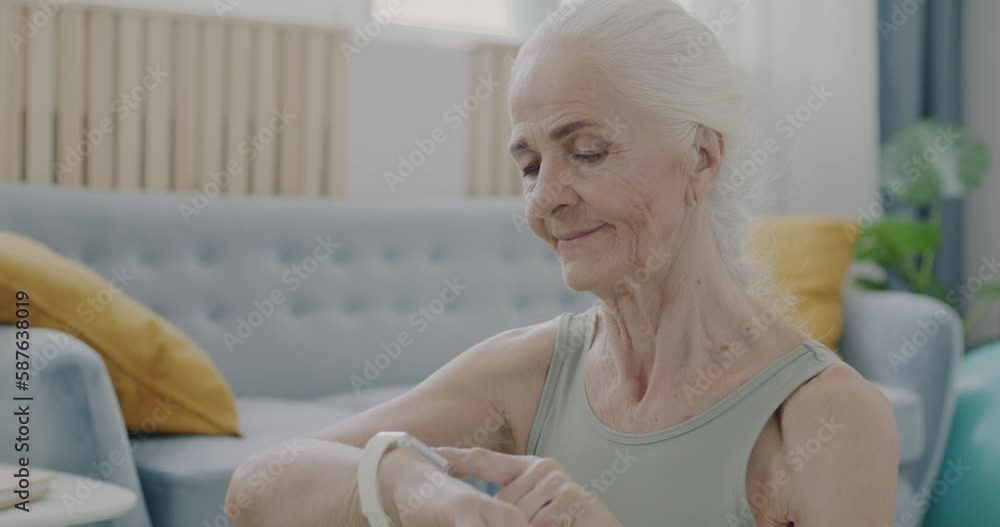 Slow motion portrait of senior sportswoman using smart watch touching display indoors at home. Modern technology and retirement concept. Slow motion portrait of senior sportswoman using smart watch touching display indoors at home. Modern technology and retirement concept.