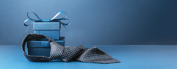 Happy Fathers Day background banner. Two blue gift boxes with ribbon bow and necktie on dark blue table. Monochrome. Gift delivery for him. Male fashion