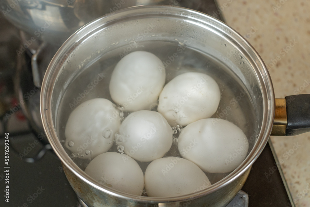 White chicken eggs are boiled in a stainless steel iron saucepan. White chicken eggs are boiled in bubbling hot water in a saucepan on a gas stove. Close-up top view White chicken eggs are boiled in a stainless steel iron saucepan. White chicken eggs are boiled in bubbling hot water in a saucepan on a gas stove. Close-up top view