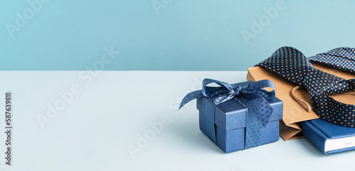 Happy Fathers Day background banner. Side view. Blue gift box and brown paper bag, necktie and agenda on pastel blue table. Corporate gift