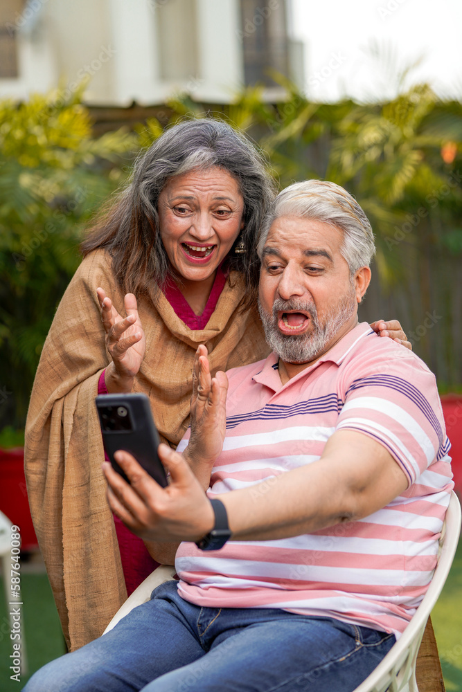Indian senior couple using smartphone and giving expression like talking on video call.