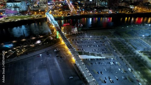 Aerial Forward Tilt Up Shot Of Illuminated John Seigenthaler Pedestrian Bridge By Parking Lot In City At Night - Nashville, Tennessee photo