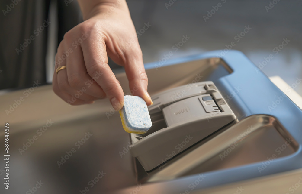 A hand puts a capsule into the container of the dishwasher. Dishwashing concept. A hand puts a capsule into the container of the dishwasher. Dishwashing concept.