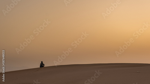 una persona contemplando el amanecer sentada sobre la arena en una duna en el desierto