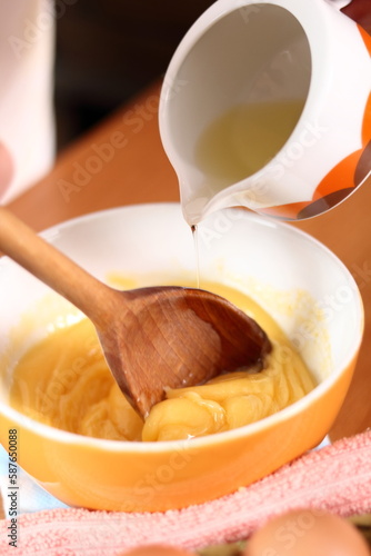 Pouring oil to an egg yolk. Making mayonnaise with a wooden spoon.