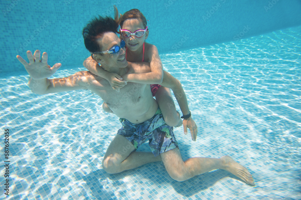 underwater photo of young dad with little girl in swimming pool