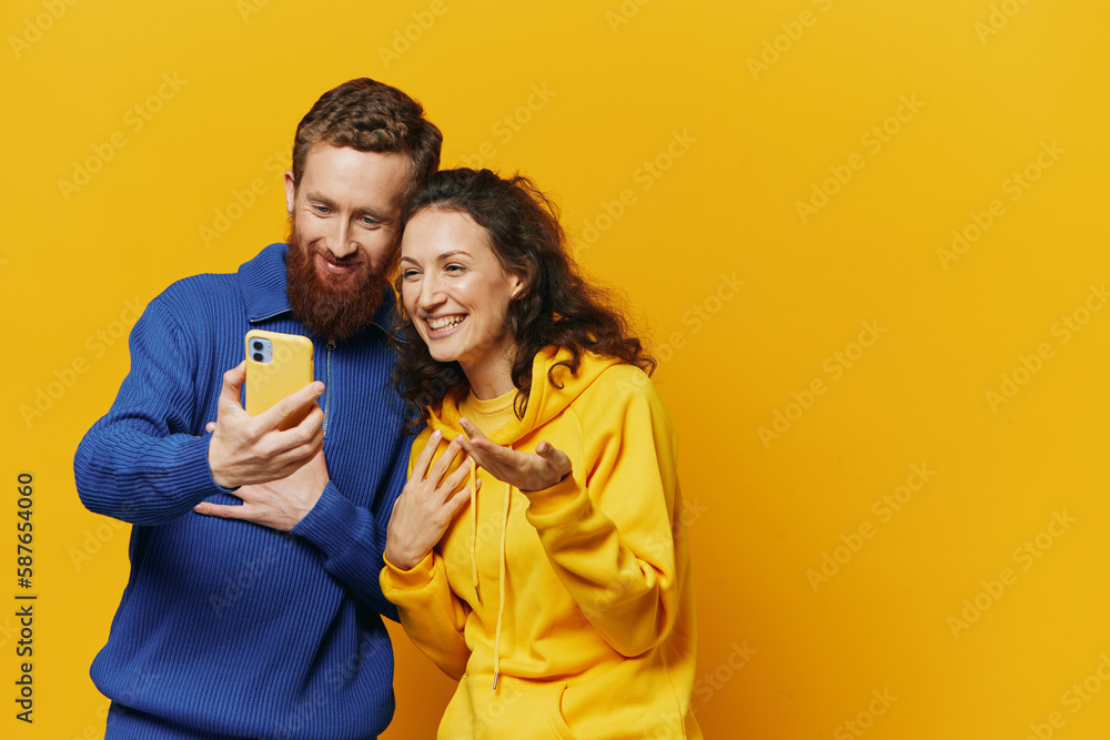 Man and woman couple smiling merrily with phone in hand social media viewing photos and videos, on yellow background, symbols signs and hand gestures, family freelancers. Man and woman couple smiling merrily with phone in hand social media viewing photos and videos, on yellow background, symbols signs and hand gestures, family freelancers.