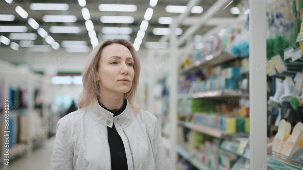A blonde woman walks through a supermarket amongst shelves of household chemicals, picking out a cleaning product. A blonde woman walks through a supermarket amongst shelves of household chemicals, picking out a cleaning product.