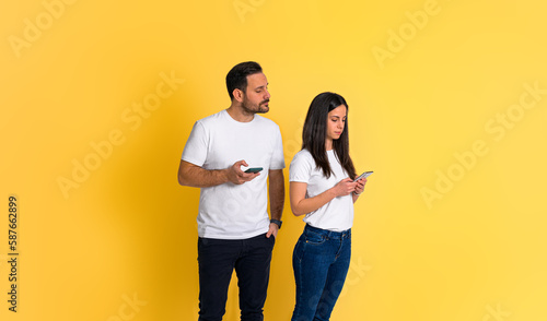 Photos Possessive young adult man peeking at girlfriend's smart phone and trying to rea