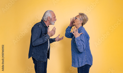 Fotografie Side view of furious senior couple dressed in blue jeans arguing and screaming a