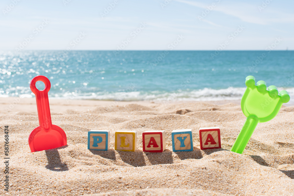 Playa (Spanish Beach) letters on cubes in the sand and ocean in the background. Copy space. Vacations background. Kids sand toys. Playa (Spanish Beach) letters on cubes in the sand and ocean in the background. Copy space. Vacations background. Kids sand toys.