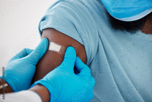 Doctor, hands and plaster on arm after vaccine with patient for safety, prevention and immunity. Healthcare, covid bandage and black man with medical professional after clinic vaccination in hospital