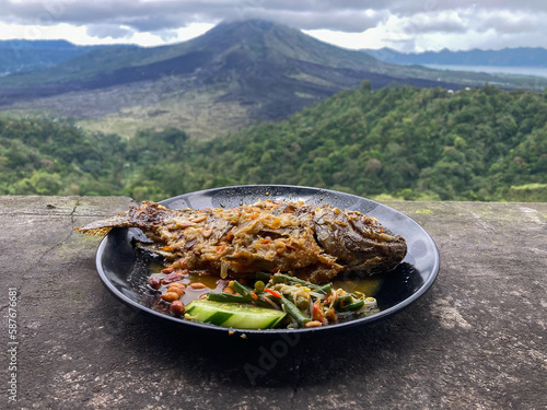 Delicious Traditional Cuisine Steamed Tilapia Fish or Ikan Mujair Nyat-nyat from Kintamani, Bali served on black plate with peanuts, vegetables, and fresh herbs photo