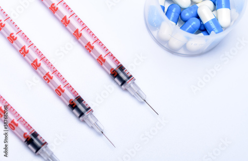 Dwie strzykawka z igłą i fiolka z lekarstwami leżące na białym tle