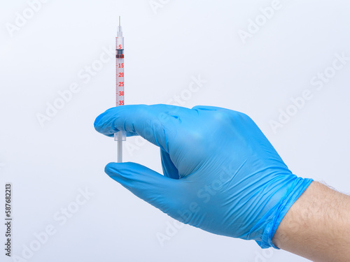 Strzykawka z igłą trzymana przez lekarza w niebieskich nitrylowych rękawiczkach 