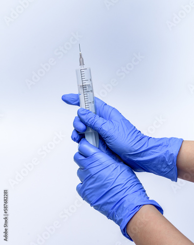 Duża, biała strzykawka z igłą trzymana w dłoniachrsez pielęgniarkę w niebieskich rękawiczkach na białym tle 