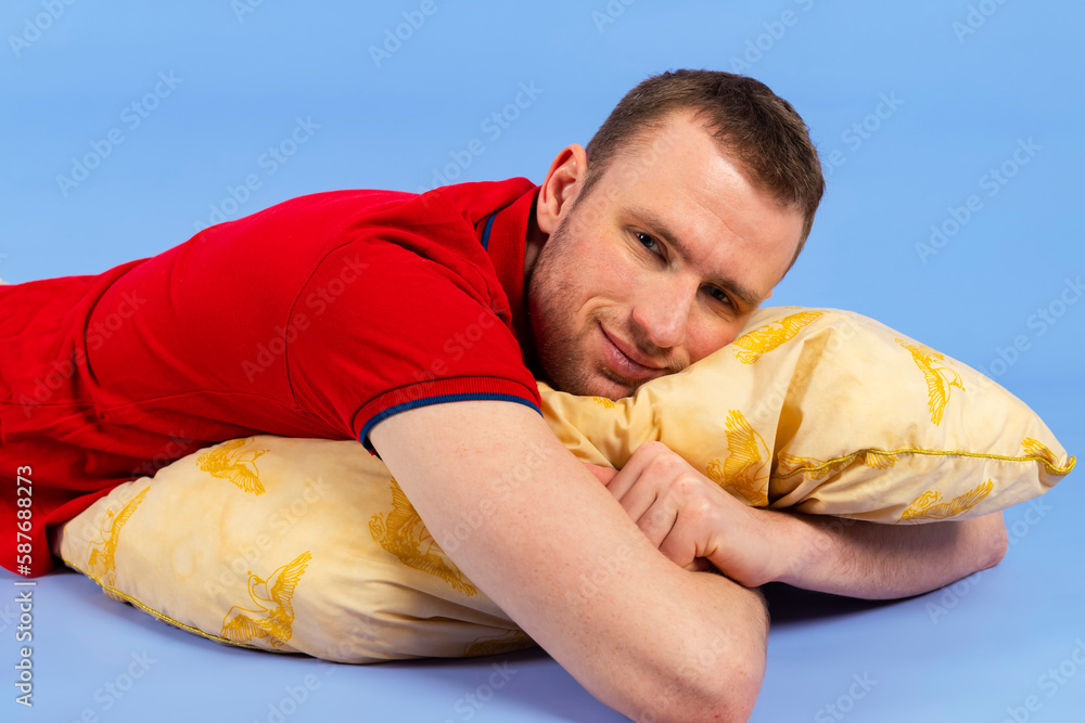 Young handsome healthy man in a red polo shirt is lying on a pillow. Isolated on blue background. Young handsome healthy man in a red polo shirt is lying on a pillow. Isolated on blue background.