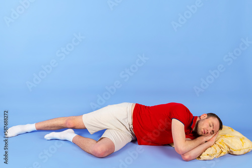 Young handsome healthy man in a red polo shirt is lying on a pillow. Isolated on blue background. full length.