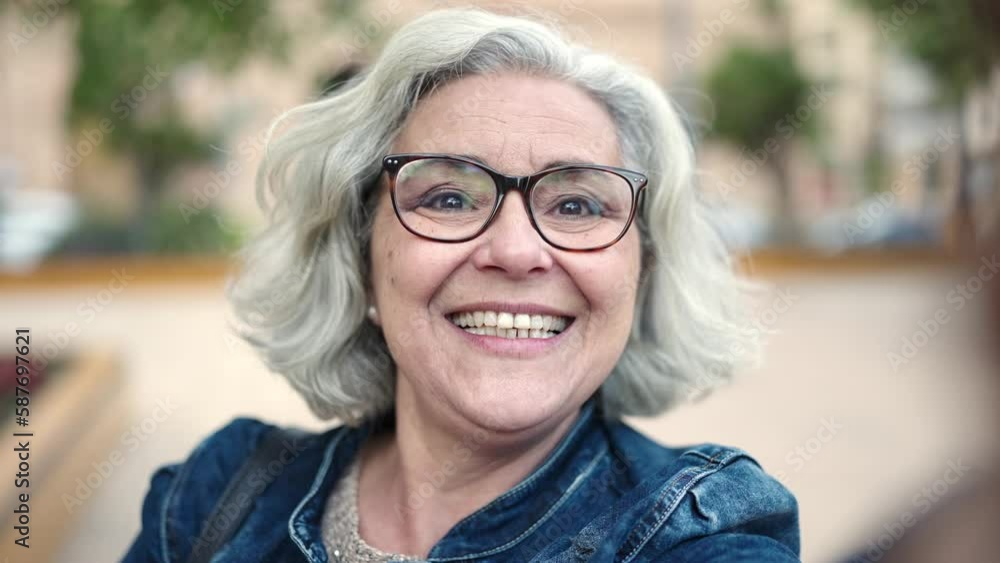 Middle age woman with grey hair smiling confident having video call at park Middle age woman with grey hair smiling confident having video call at park
