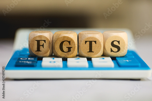 A sigla FGTS para Fundo de Garantia do Tempo de Serviço escrita em dados de madeira que estão sobre uma calculadora azul. Economia brasileira, trabalho, trabalhador, empregado. photo