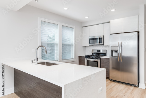 A modern kitchen with stainless steel appliances  a waterfall granite island  a light hardwood floor  and a patterned tile backsplash. No names or brands.