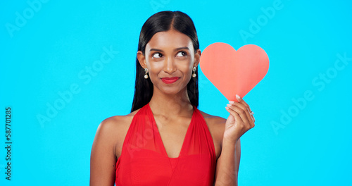 Thinking, happy or woman with heart paper sign for Valentines Day, studio care and emoji love icon, symbol or poster. Portrait, female beauty or person contemplating secret admirer on blue background