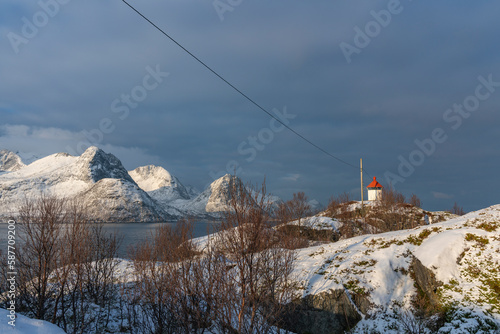 Panorama mit Leuchtturm im Øyfjorden mit schneebedeckten Bergen von Senja, genannt Segla, Kongan und Skultran. interessante Winterstimmung mit blauem und bewölktem Himmel und steilen felsige Bergen photo