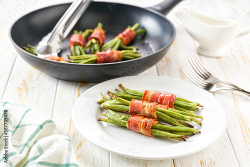 Pan with fried appetizer, bundles of green beans wrapped in bacon on wooden table, top view.