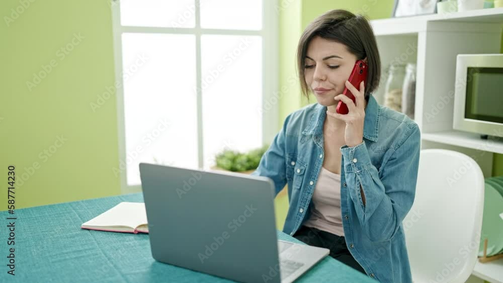Young caucasian woman talking on smartphone using laptop at home Young caucasian woman talking on smartphone using laptop at home