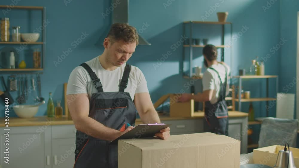 Worker of Moving Company Using Clipboard to Check List of Customers' Things for Moving. Travel Insurance. Psychological Aspects of Moving. Intercity Moving Worker of Moving Company Using Clipboard to Check List of Customers' Things for Moving. Travel Insurance. Psychological Aspects of Moving. Intercity Moving