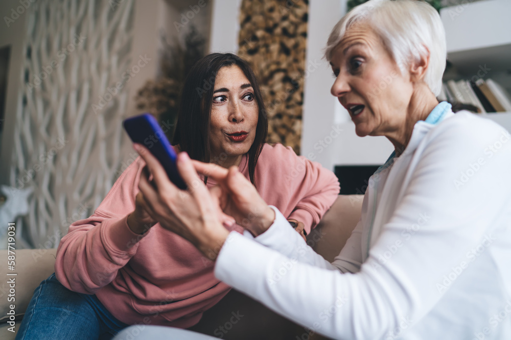Shocked senior diverse women discussing information on mobile phone Shocked senior diverse women discussing information on mobile phone