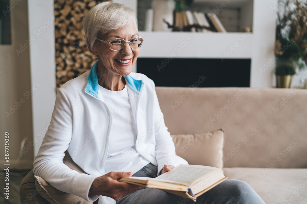 Cheerful senior woman sitting on sofa and reading book at home Cheerful senior woman sitting on sofa and reading book at home