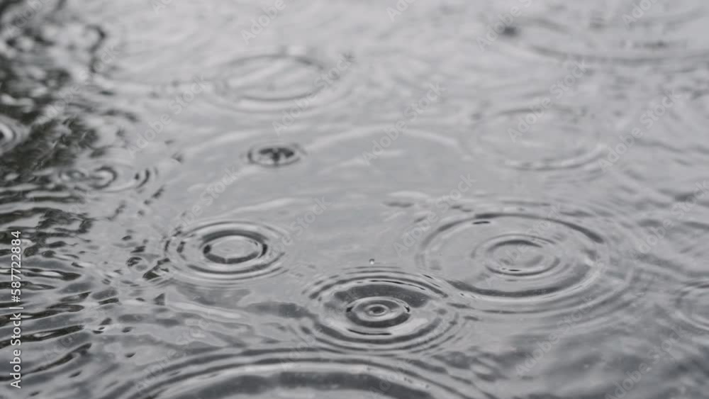 Slow motion closeup of summer heavy rain drops falling into puddles on asphalt Slow motion closeup of summer heavy rain drops falling into puddles on asphalt
