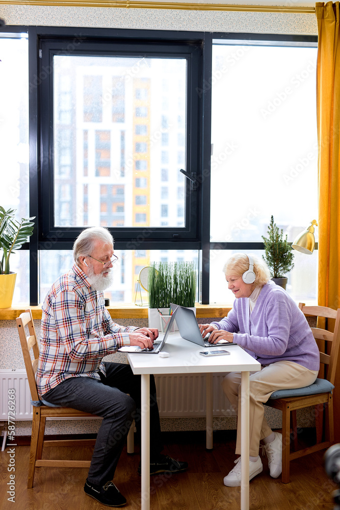 Mature Caucasian People Using Laptop Working Or Studying At Home, Websurfing In Cozy Room. Older Couple Sit Opposite Of Each Other Browsing Internet On Laptop Reading Online News On Weekend Mature Caucasian People Using Laptop Working Or Studying At Home, Websurfing In Cozy Room. Older Couple Sit Opposite Of Each Other Browsing Internet On Laptop Reading Online News On Weekend