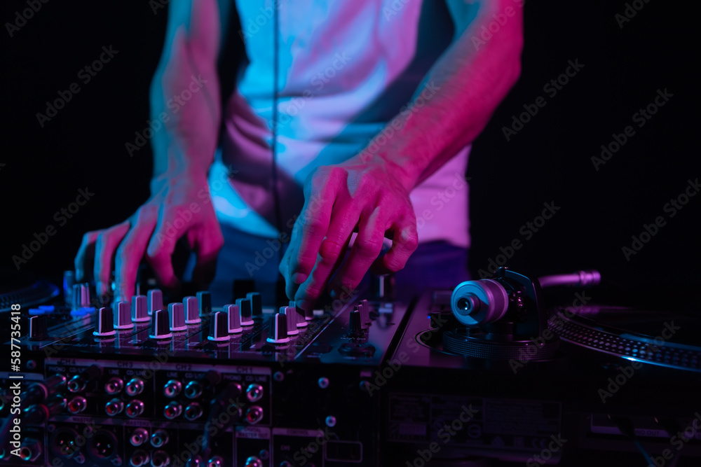 Hands of club DJ mixing music. Professional disc jockey plays set with sound mixer and vinyl turntables Hands of club DJ mixing music. Professional disc jockey plays set with sound mixer and vinyl turntables