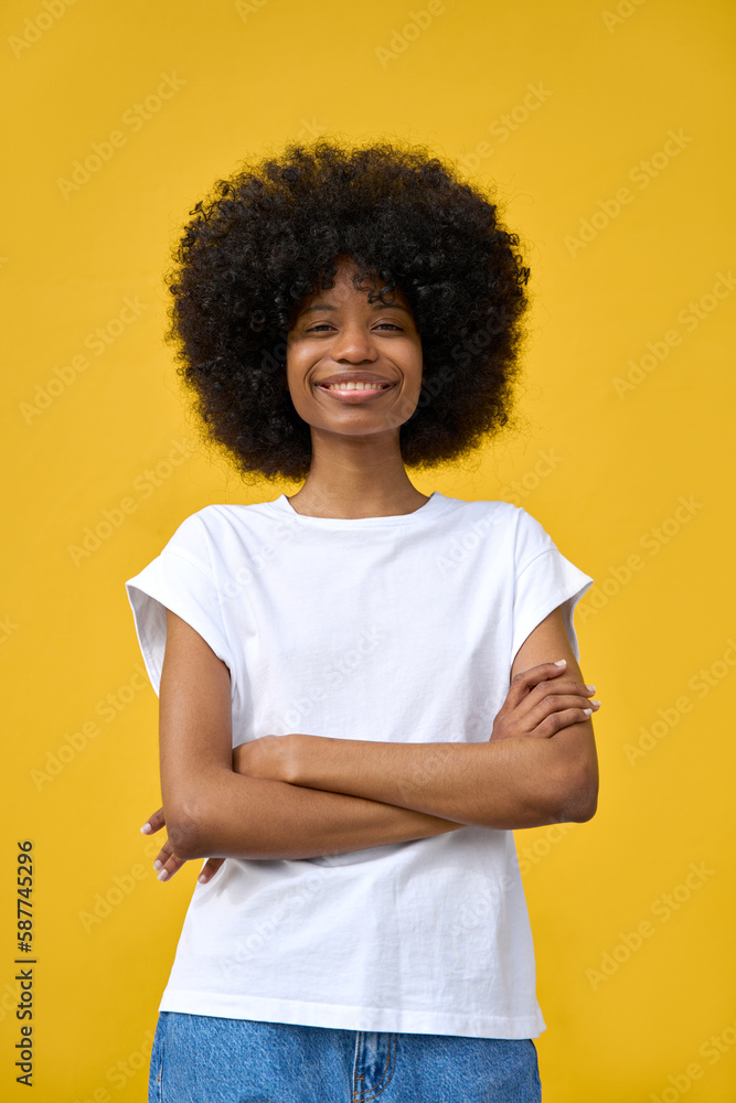 Young stylish woman model pose in white t-shirt in front of a yellow background looking at camera. Beautiful afro hair african american girl in trendy clothes stands with crossed arms. Vertical photo