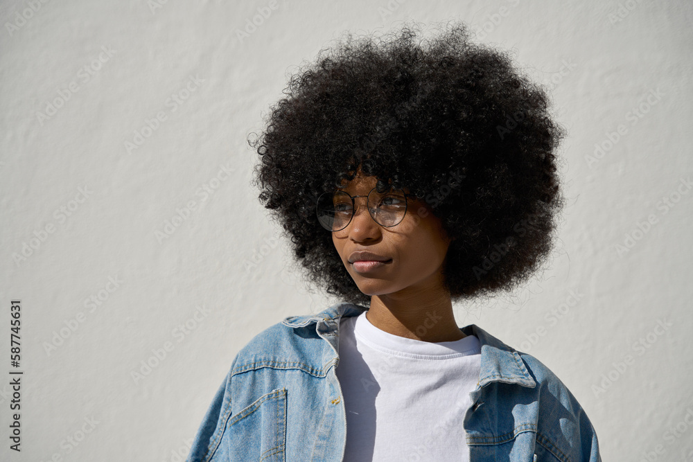 A portrait headshot of a young happy stylish woman with a big afro hairstyle and in eyeglasses on white background. A cool african american female hipster girl in trendy jeans jacket looking aside. A portrait headshot of a young happy stylish woman with a big afro hairstyle and in eyeglasses on white background. A cool african american female hipster girl in trendy jeans jacket looking aside.
