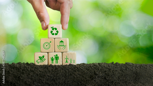 Hand holding a wooden cube with abbreviation ESG standing icon. On a green background, environmental, social and governance concepts. Sustainable Organization Development