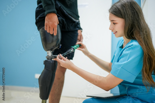 Female physiotherapist helping young man with prosthetic leg..Nurse helping man walk with prosthetic leg..Young disabled man using orthopedic equipment to walk