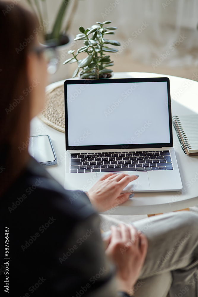 Mockup white screen laptop and mobile phone woman using computer sitting at table at home, back view Mockup white screen laptop and mobile phone woman using computer sitting at table at home, back view