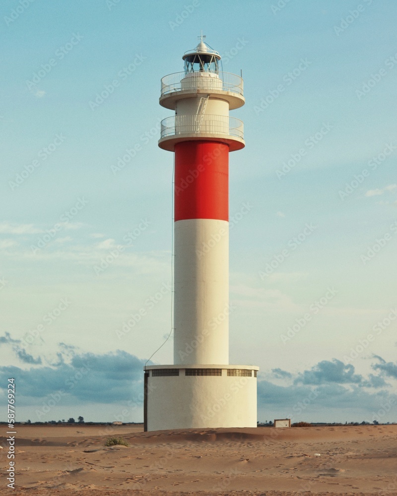 White lighthouse with red line on the beach and blue sky
