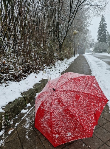 Fototapeta Naklejka Na Ścianę i Meble -  Close up of red umbrella in snow with frost and snowflakes. Street and the first snowfall of the winter season