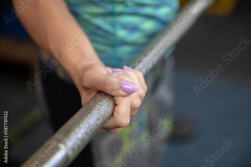 Close-up of a woman's hand clenched on a metal exercise barbell