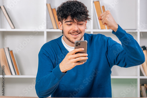 young student at desk excited looking at smartphone photo