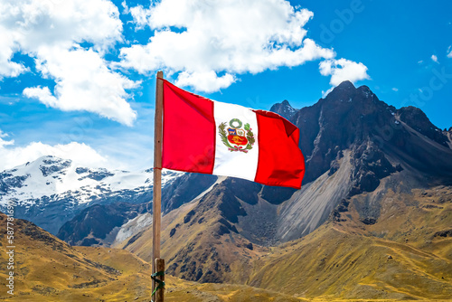 The Peruvian flag waving proudly in the wind against the backdrop of the majestic La Raya mountain range, with the snow-covered Chimboya peak adding to the impressive scenic view of the Andes in June.