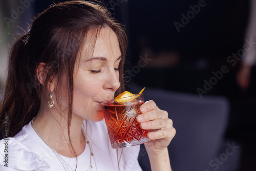 a girl drinks a negroni cocktail on the terrace of a modern restaurant